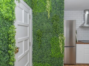 Eine Küche mit einer weißen Tür, einem Edelstahlkühlschrank und einer Wand, die mit Grünpflanzen bewachsen ist.
