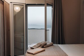 A hotel room with a bed, a view of the sea, and a sliding door leading to an outdoor area. - Magic View Apartment (Zakynthos)
