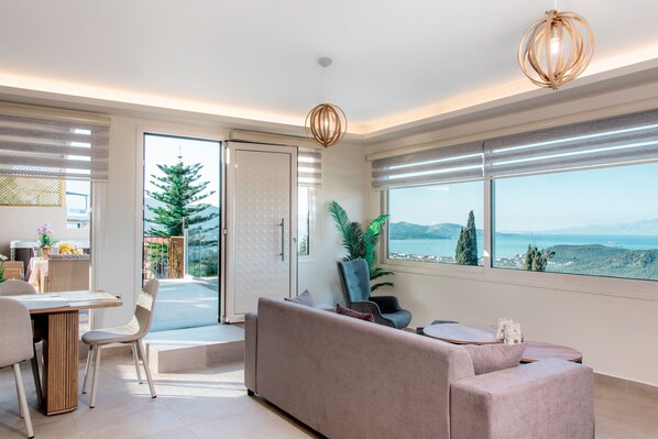 A modern living room with a sofa, chairs, a dining table, and a view of the sea. - Magic View Apartment (Zakynthos)
