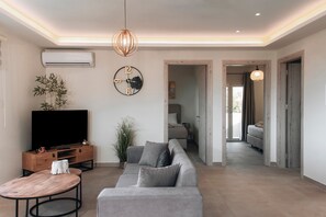 A modern living room with a grey sofa, a wooden coffee table, a TV on a wooden stand, and a wall-mounted clock. - Magic View Apartment (Zakynthos)