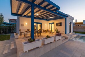 A modern outdoor patio with a covered seating area, a pool, and potted plants. - Serenity Villa Thalassa (Kolympia)