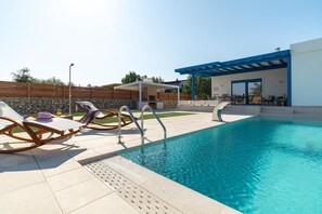 A swimming pool with lounge chairs and a covered seating area. - Serenity Villa Thalassa (Kolympia)