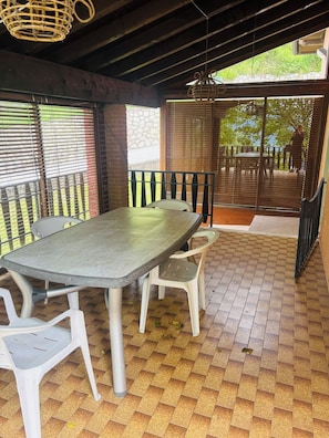Une terrasse extérieure avec une table et des chaises, un espace couvert avec un plafond, et une vue sur l’extérieur.