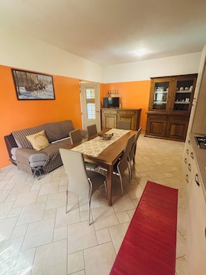 Un espace repas comprenant une table en bois, des chaises, un canapé et un coin cuisine avec des placards et une cuisinière.