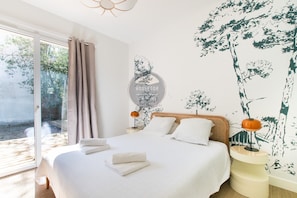 A bedroom with a large bed, a nightstand, a lamp, and a wall mural. - Villa Goxoki - Capbreton - City Center - Garden (Capbreton)