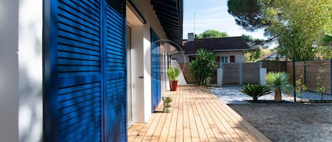 A wooden deck leading to a building with blue shutters, a small garden with plants, and a fence.