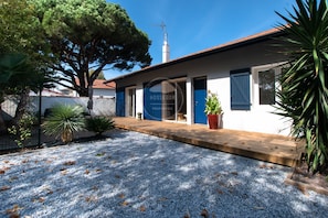 Une propriété dotée d’une allée en gravier, d’une terrasse en bois et d’un grand arbre.