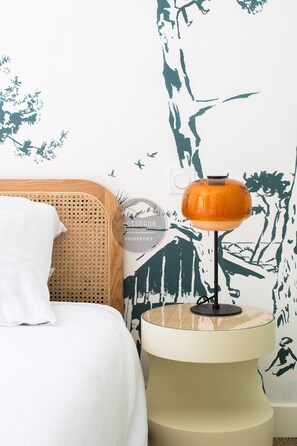 A room with a bed, a rattan chair, a round table with a lamp, and a wall with a nature-themed mural. - Villa Goxoki - Capbreton - City Center - Garden (Capbreton)