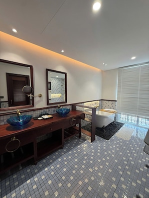 A modern bathroom with a wooden vanity, two blue glass sinks, a large mirror, and a bathtub. - VESTA BOUTIQUE HOTEL PHU QUOC (Dac Khu Phu Quoc)