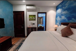 A hotel room with a bed, a desk, a chair, a TV, and a wall with a blue mural. - VESTA BOUTIQUE HOTEL PHU QUOC (Dac Khu Phu Quoc)