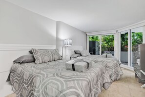 A modern bedroom with a large bed, a bedside table, and a view of greenery through the glass door. - Poolside 2BR | Workspace for two | Gym access (Miami)