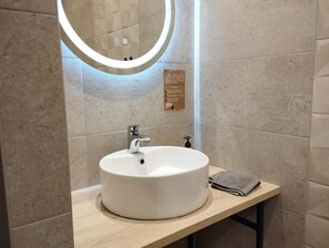 A bathroom with a round mirror, a sink, and a towel on the counter. - Apartment 'Coliving Des Moulins Sur Crémieu' with Wi-Fi and Air Conditioning (Crémieu)