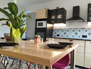 A modern kitchen with a wooden dining table, a microwave, and a black range hood. - Apartment 'Coliving Des Moulins Sur Crémieu' with Wi-Fi and Air Conditioning (Crémieu)
