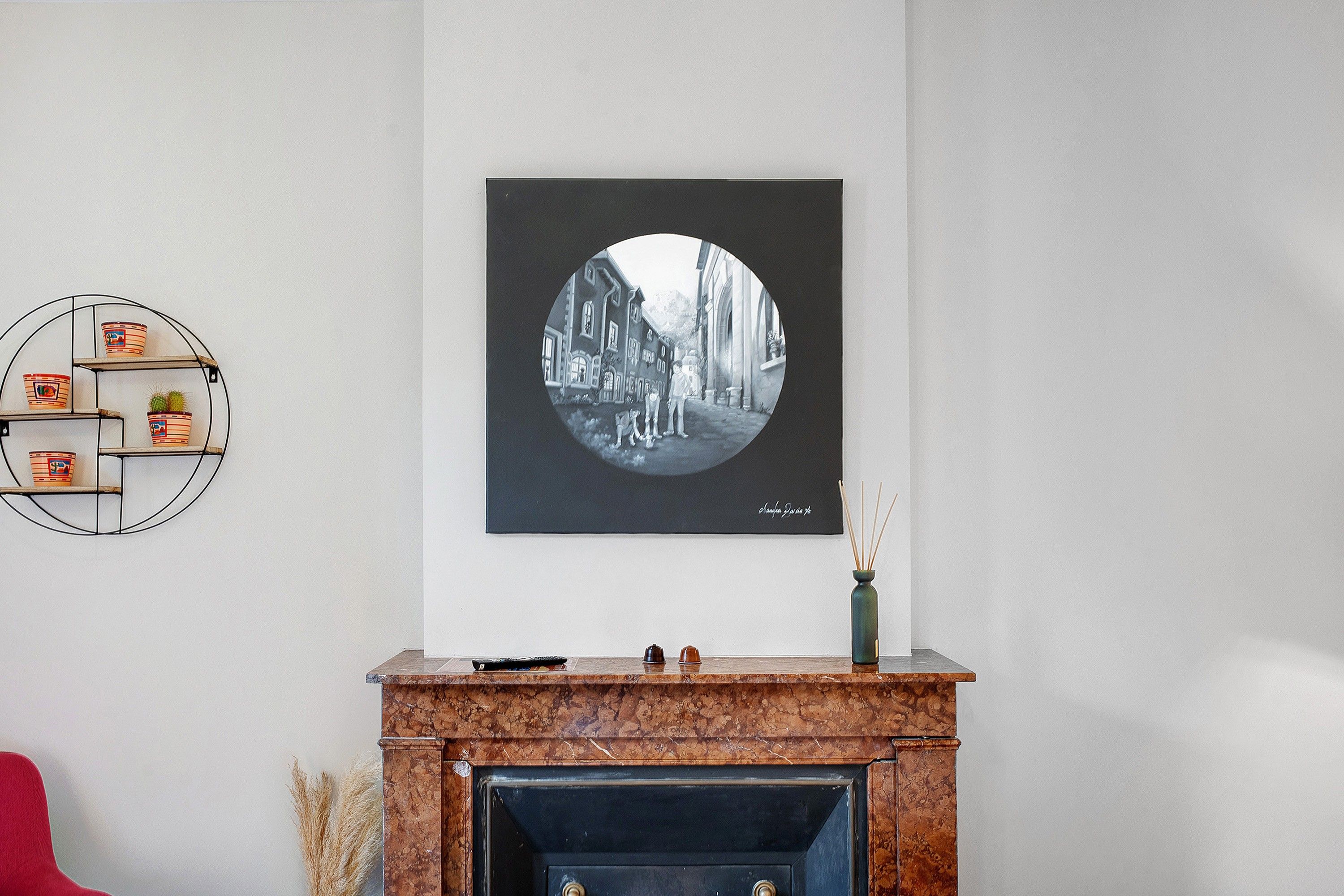 Een woonkamer met een open haard, een zwart-wit foto in een lijst en een ronde plank met decoratieve objecten.