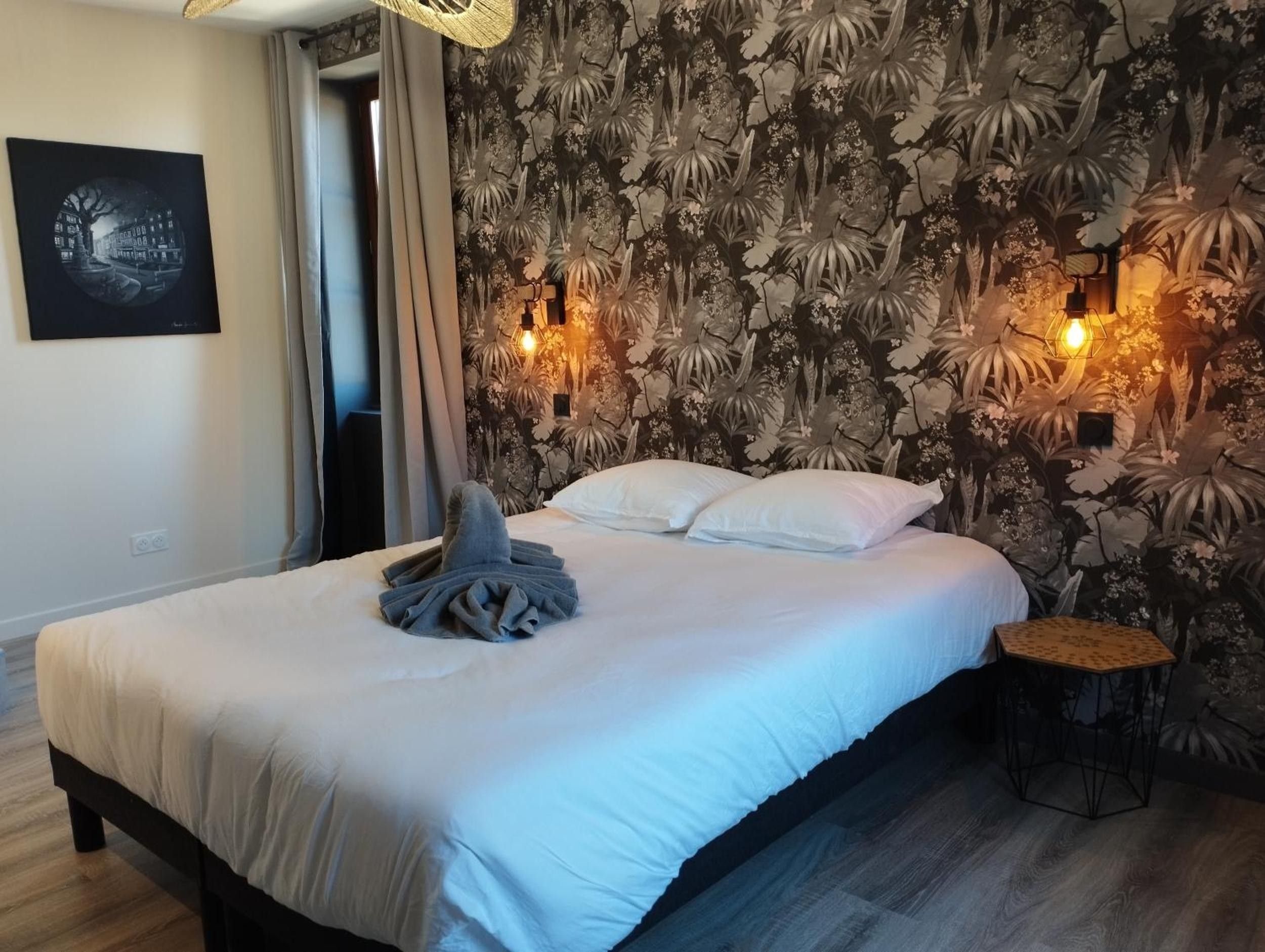 A hotel room with a bed, a wall with a floral pattern, and two wall-mounted lights.