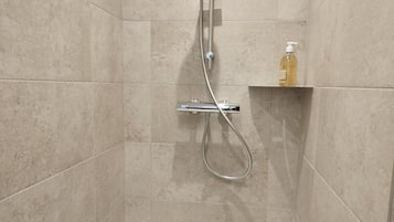 A shower area with a handheld showerhead and a bottle of soap on a shelf.