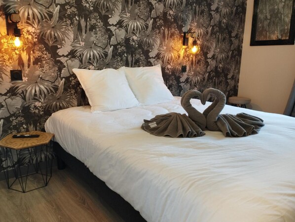 Habitación de hotel con una cama, dos luces fijadas a la pared, un control remoto sobre una mesita de noche y una decoración de toallas con forma de cisne.