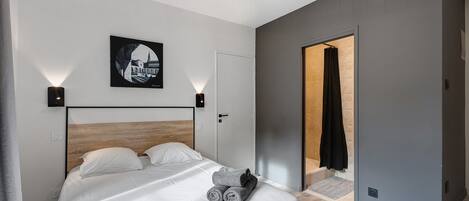 Un dormitorio moderno con cabecera de madera, cama con ropa blanca, lámpara de pared e imagen enmarcada.
