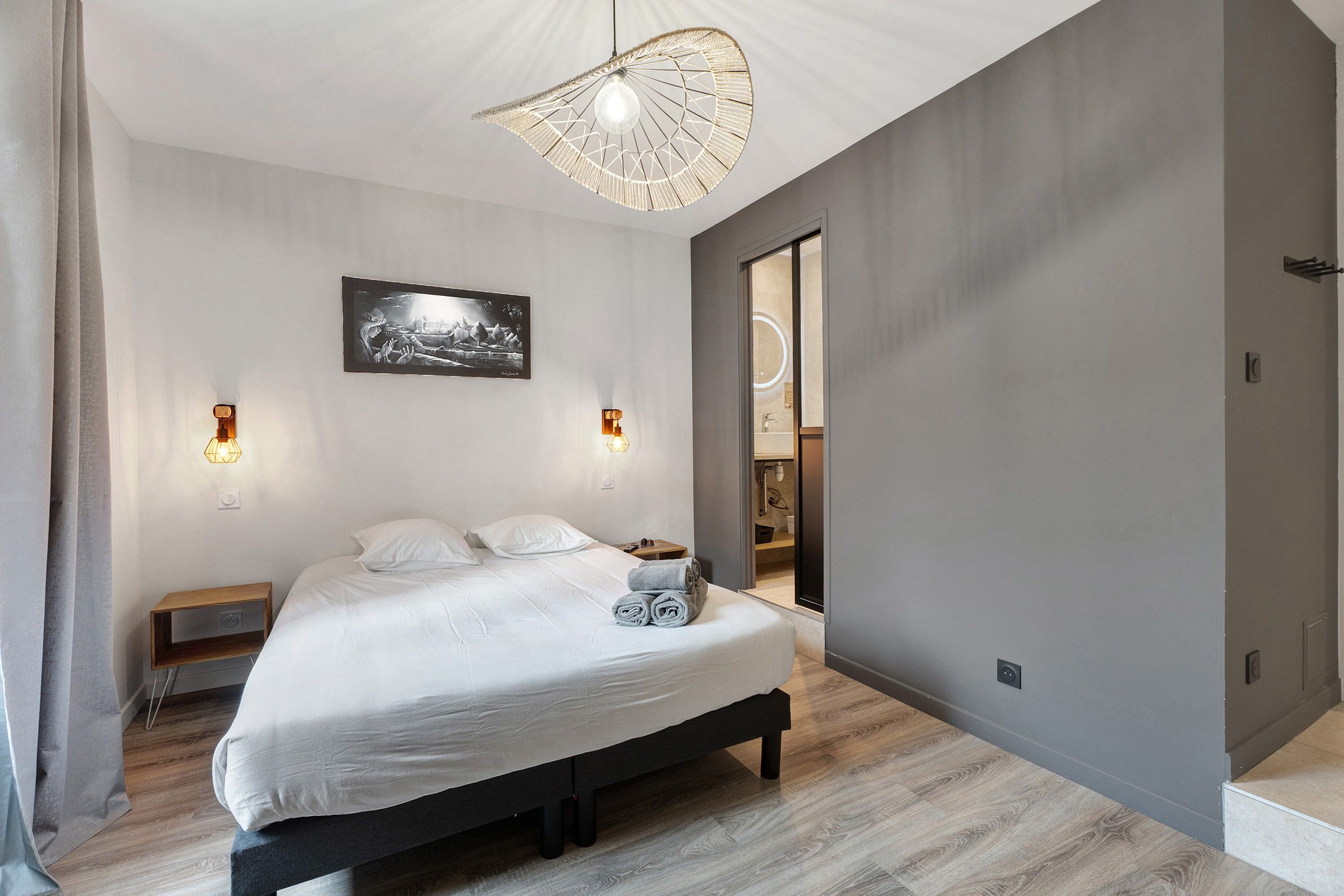 Een moderne slaapkamer met een bed, bedlampen, een aan de muur bevestigd schilderij en een deur naar een badkamer.