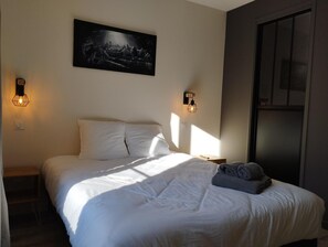 Une chambre à coucher avec un lit, deux lampes fixées au mur, un tableau au-dessus du lit et une fenêtre sur le côté droit.
