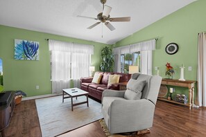 A living room with a ceiling fan, a brown leather sofa, a gray armchair, a wooden coffee table, and a green wall. - 2/2 Well Maintained quiet retreat in the Village of Duval (The Villages)