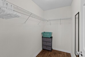 A small, well-lit room with white walls, a wooden floor, a grey dresser with drawers, and a teal basket on top. There are metal wire shelves on the walls and a door with a black frame. - 2/2 Well Maintained quiet retreat in the Village of Duval (The Villages)