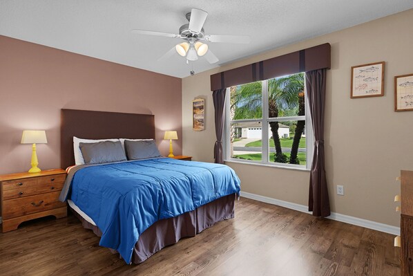 A bedroom with a bed, two bedside tables, a ceiling fan, a window with curtains, and wall art. - 2/2 Well Maintained quiet retreat in the Village of Duval (The Villages)