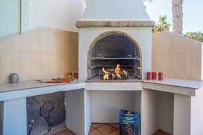 An outdoor brick oven barbecue area with a stone wall, a shelf with tools, and a bag of charcoal. - Villa Buena Vida - Four Bedroom Villa, Sleeps 8 (Playa Blanca)