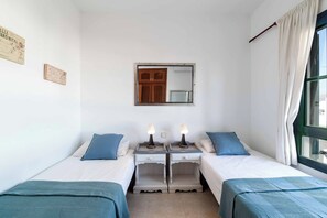 A room with two beds, a small table, a mirror, and a window with curtains. - Villa Buena Vida - Four Bedroom Villa, Sleeps 8 (Playa Blanca)