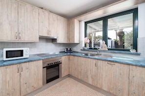 A kitchen with wooden cabinets, a microwave, a stove, and a window with a view of outdoor plants. - Villa Buena Vida - Four Bedroom Villa, Sleeps 8 (Playa Blanca)