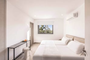 Ein modernes Schlafzimmer mit Bett, Nachttischen, einem Schreibtisch und einem Fenster mit Blick auf Bäume.