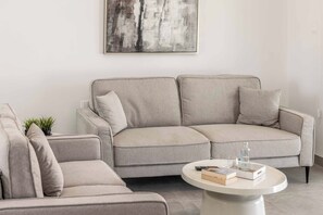 A neutral-toned sofa with a matching ottoman and a small table with books and a bottle. - Villa Galazio - Three Bedroom Villa, Sleeps 6 (Argaka)