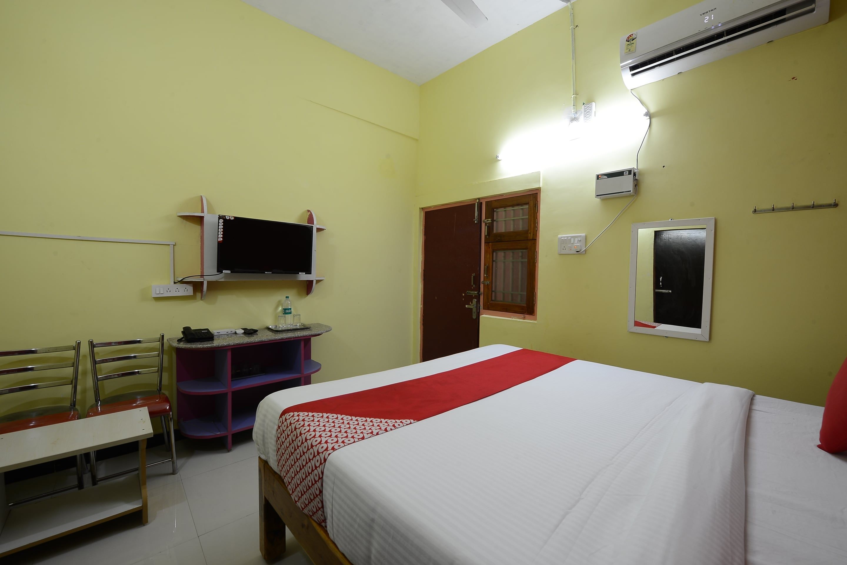 Una habitación de hotel con una cama, un escritorio, una silla, un televisor y un equipo de aire acondicionado.