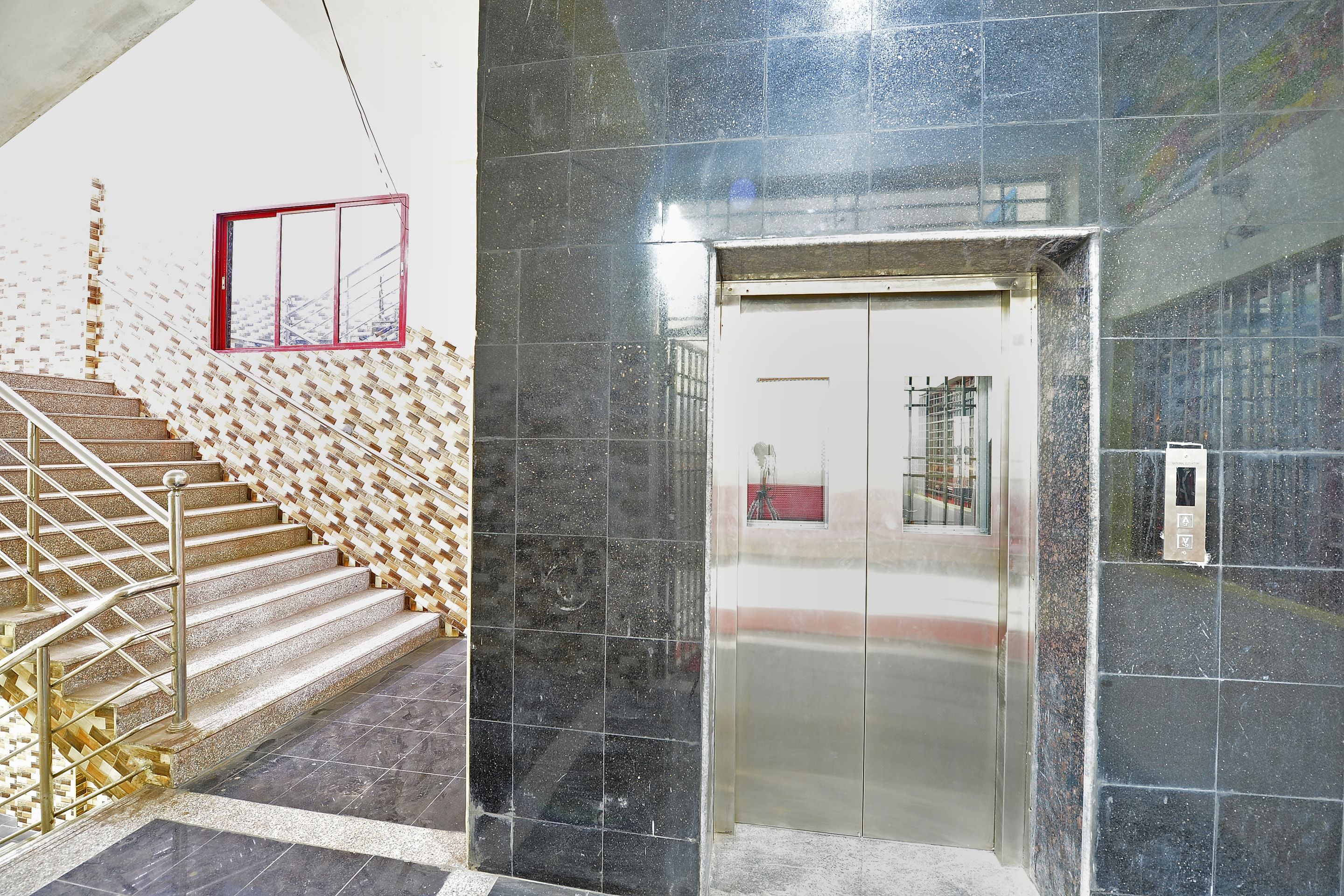 Una escalera, un ascensor metálico y un ventanal con marco rojo.