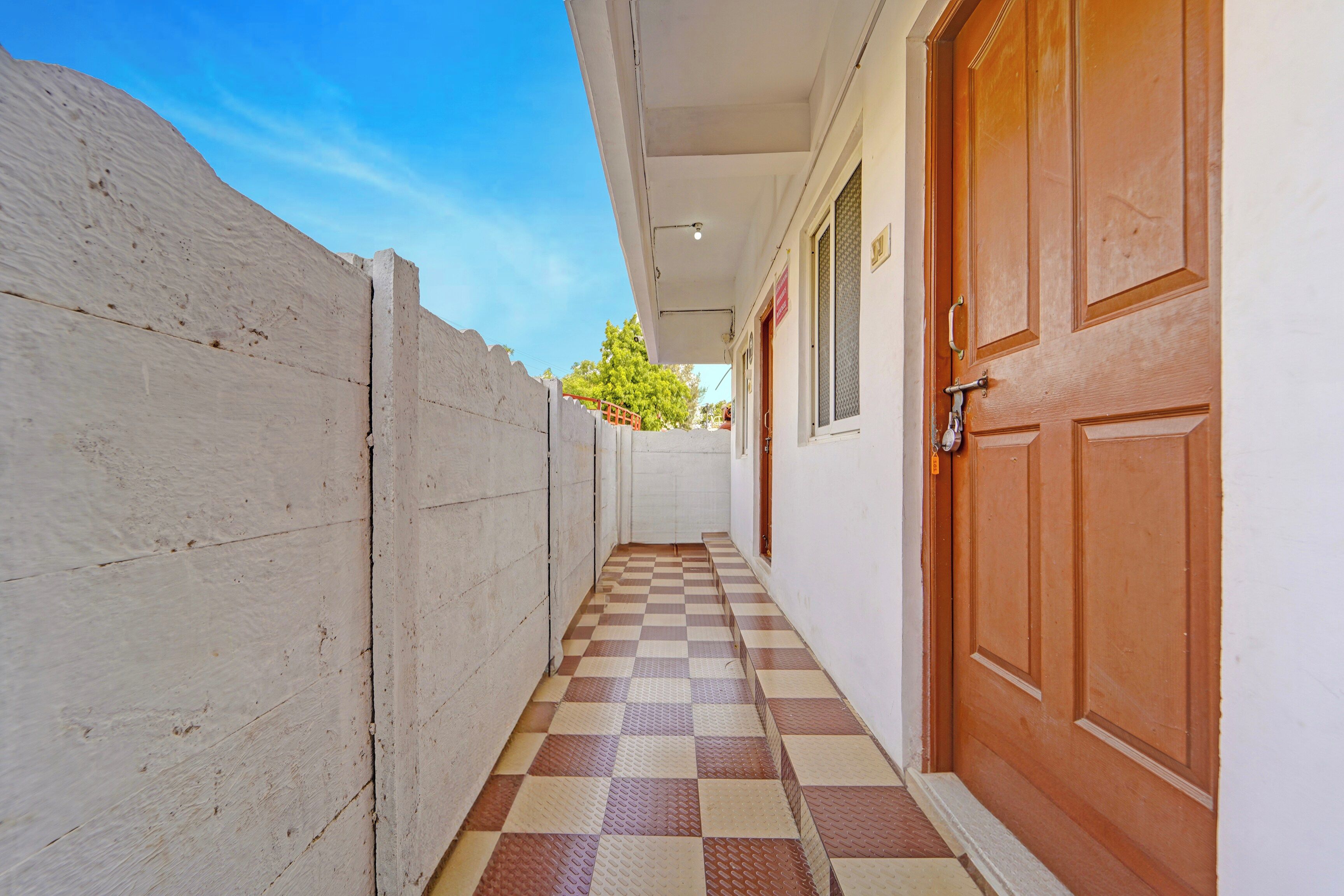 A narrow hallway with a checkered floor, a white wall, and a wooden door.