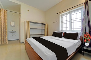Een hotelkamer met een bed, een nachtkastje met een bloevas, een raam met uitzicht en een badkamer met een wastafel en spiegel.