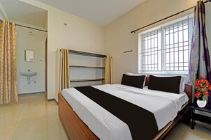 A hotel room with a bed, a bedside table with a vase of flowers, a window with a view, and a bathroom with a sink and mirror.