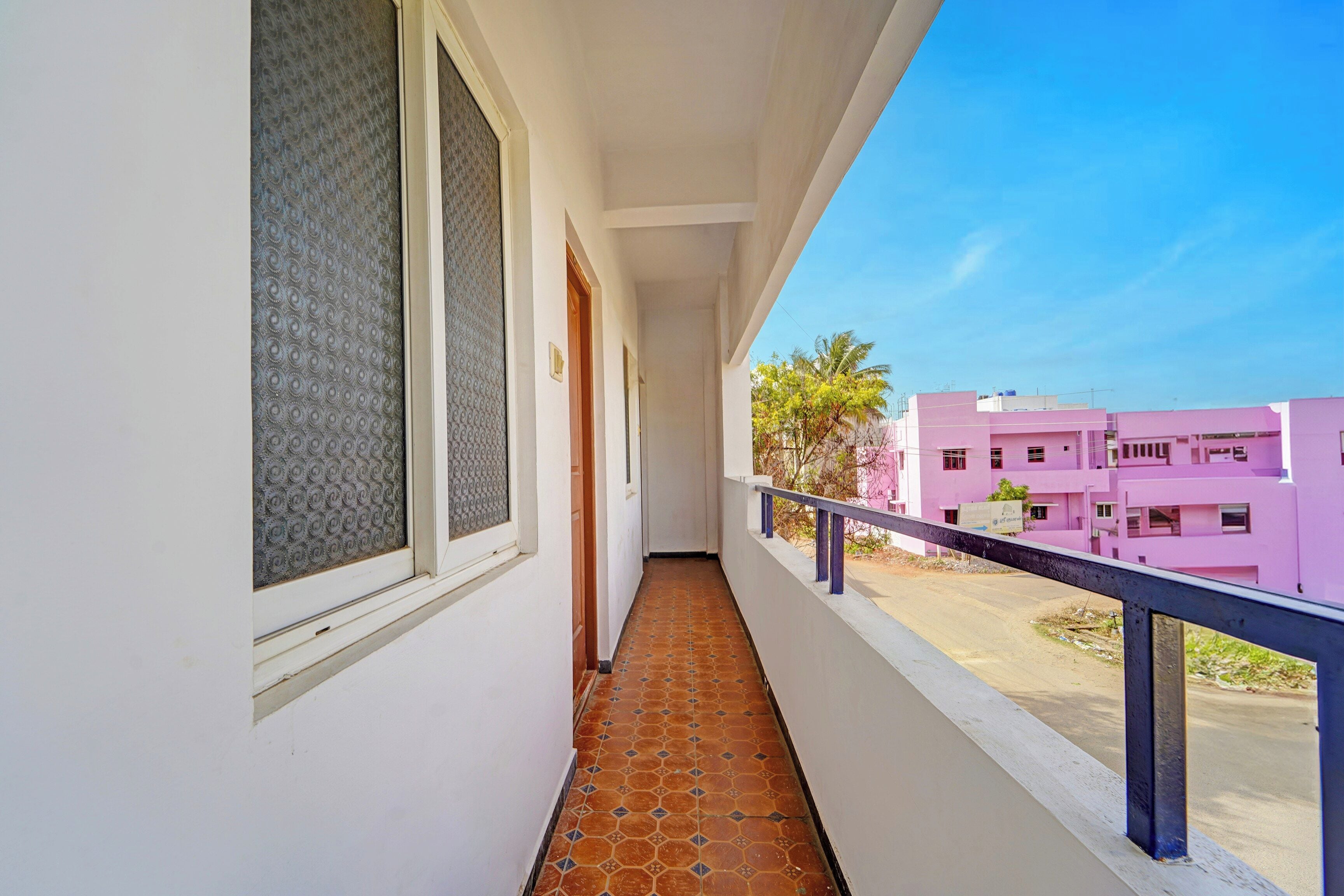 A balcony with a tiled floor, a railing, and a view of pink buildings in the distance.