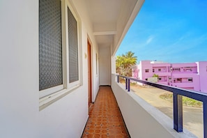 A balcony with a tiled floor, a railing, and a view of pink buildings in the distance.