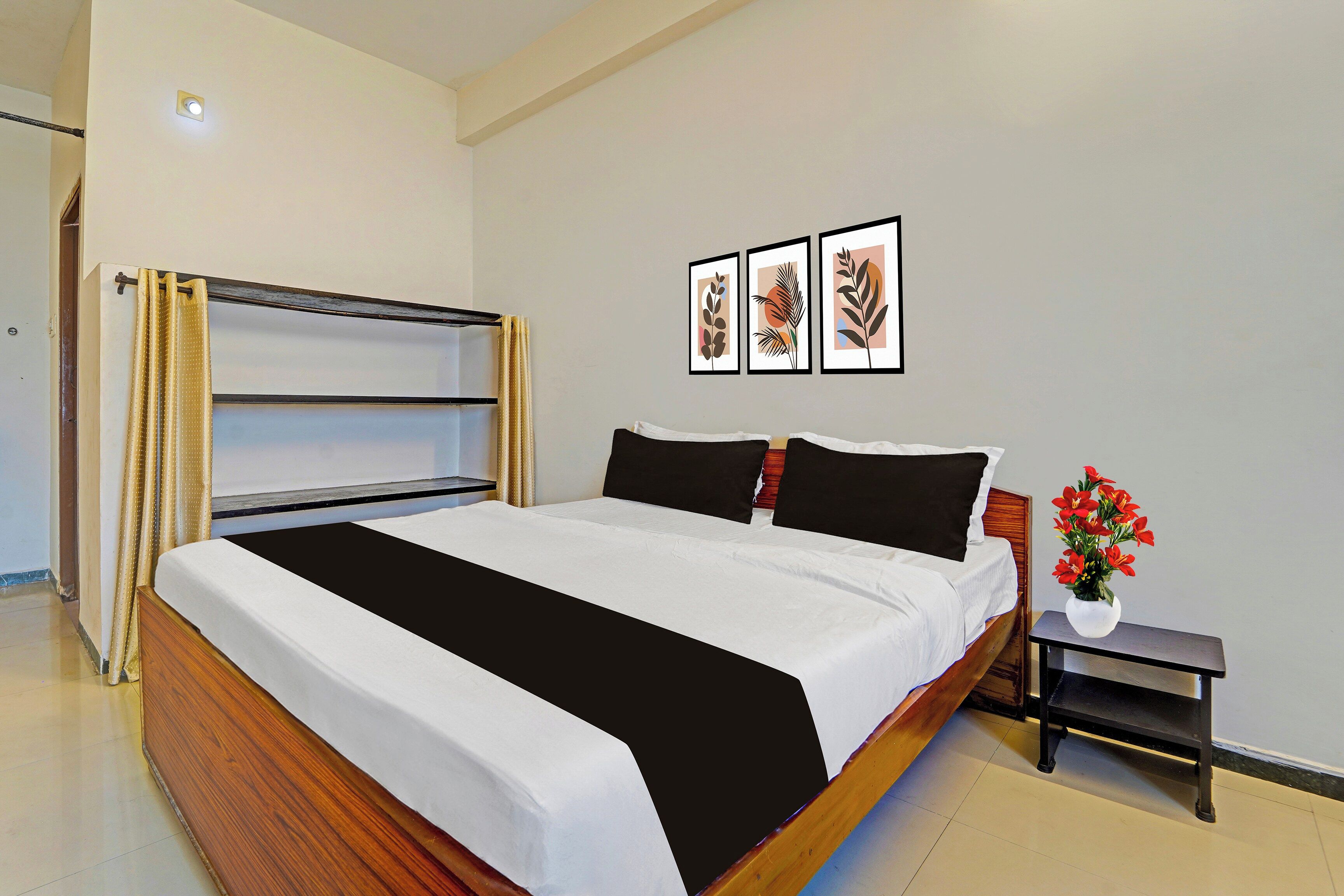 Un dormitorio con cama, mesita de noche, estante en la pared y ventana con cortinas.