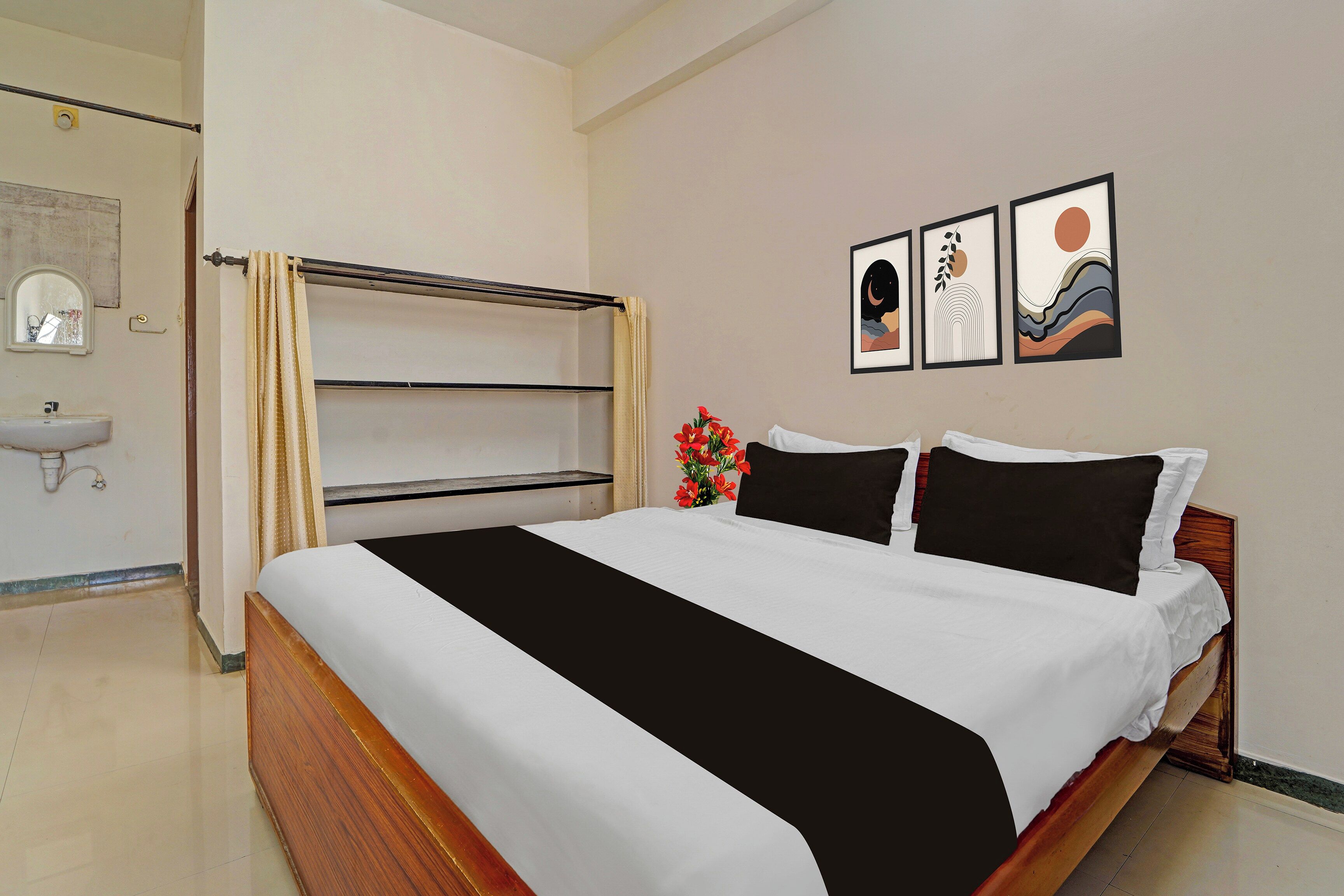A hotel room with a bed, a nightstand, a mirror, a sink, and artwork on the wall.