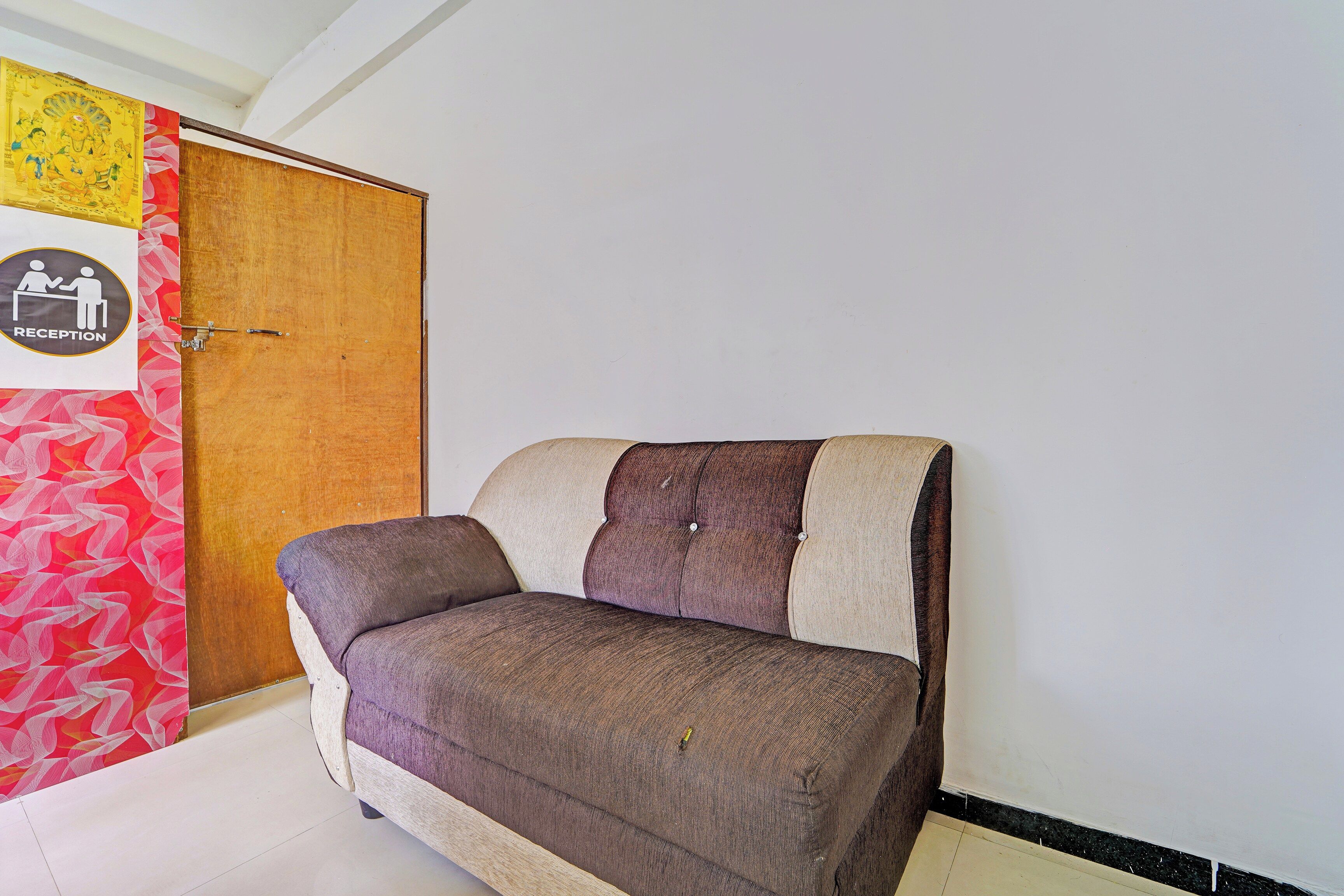 A room with a wooden door, a reception sign, and a sofa against the wall.
