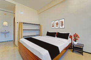 Een hotelkamer met een bed, een nachtkastje met een bloevas, een wastafel aan de muur en kunstwerken in lijsten.