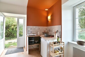 Una cocina compacta con horno integrado, cafetera y estante de madera con frascos.