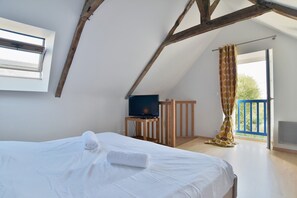 Ein Schlafzimmer mit einem Bett, einem Fernseher auf einem Holzständer, einem Fenster mit Jalousien und einem Balkon mit Vorhang.