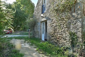 Ein Gebäude aus Stein mit Tür und Fenster, umgeben von Grünpflanzen und einem Weg.