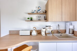 A modern kitchen with wooden cabinets, a sink, a coffee machine, a kettle, and decorative items on shelves. - Villa La Chantyviere - Piscine Privée, Pool House (Sainte-Maxime)