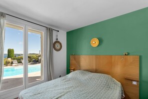 Ein Schlafzimmer mit einem großen Bett, Blick auf einen Swimmingpool und einer grünen Wand.