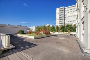 A parking lot with a building on the right and trees in the background. - L'Escale Rouennaise - Proche station de Métro (Rouen)