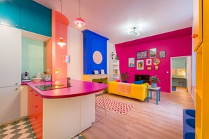 Eine moderne Küche mit einer zentralen Kochinsel, ein Essbereich mit gelbem Sofa und ein Wohnzimmer mit Kamin.